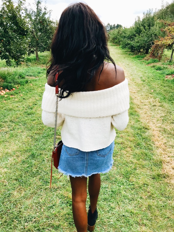 backw-hair-curles-sweater-walking-outside-fall-season-skirt-denim-orchard